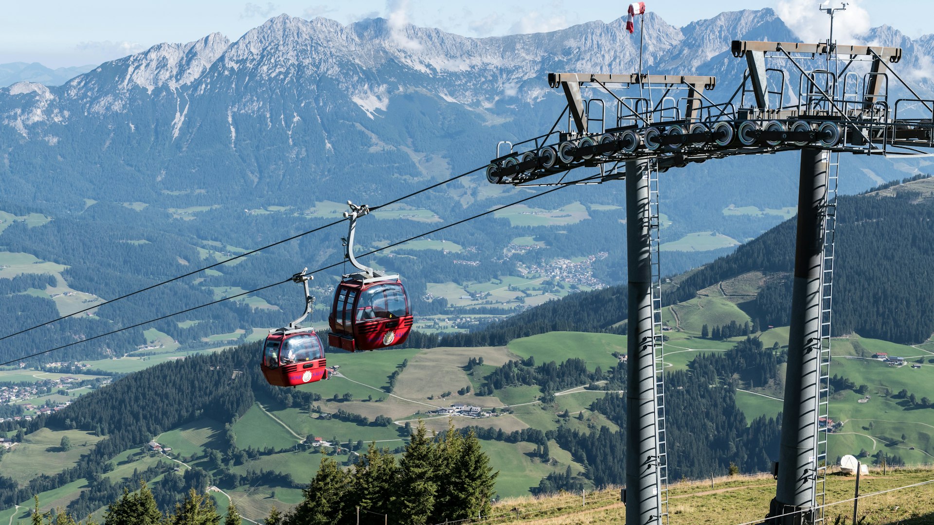 Two red gondolas ascend a mountain cableway.